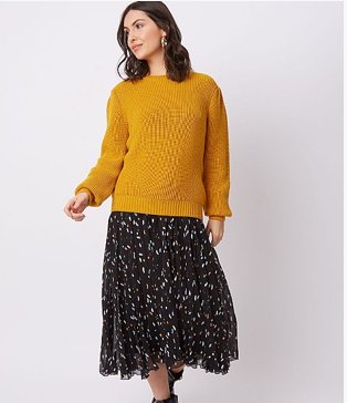 Woman wearing a mustard yellow pleated sleeve jumper with a black terrazzo patterned skirt