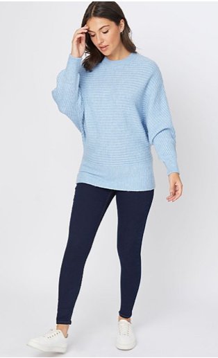 Woman wearing Wonderfit dark wash skinny jeans, white trainers and a pale blue ribbed batwing jumper