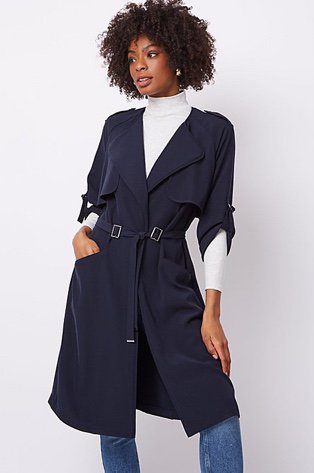 Woman in a navy belted longline trench coat over a white high neck jumper and jeans