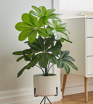 An artifical plant in a white planter on a black metal stand