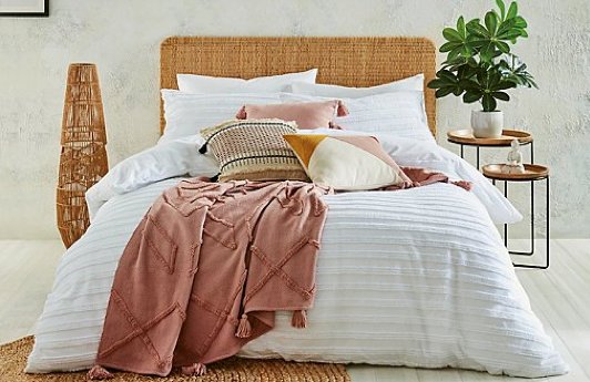 A double bed with a white striped duvet set, a selection of pink, white and stone accent cushions and a pink throw