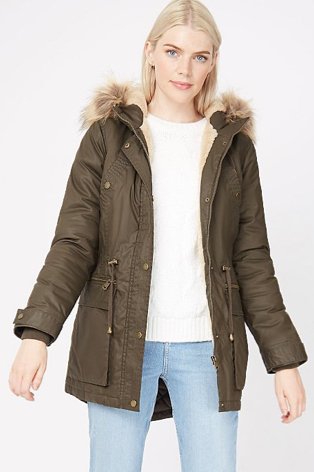 A woman wearing light wash jeans, a cream jumper and a khaki parka with faux fur trim