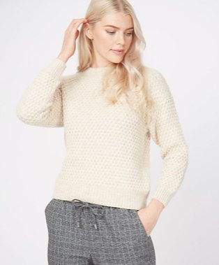 A woman wearing a cream honeycomb knit jumper with grey trousers