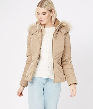 A woman wearing light wash jeans, a white jumper and a stone faux fur collar padded jacket