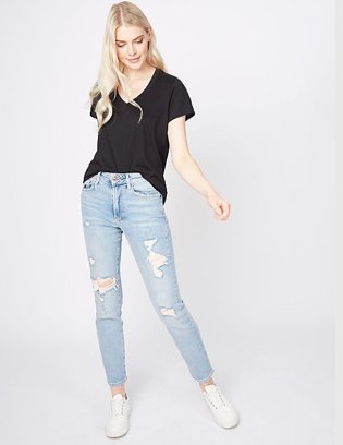 Blonde woman posing wearing black V-neck t-shirt, light blue ripped jeans and white trainers.