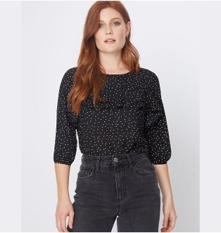Red haired woman poses wearing black sheer printed blouse tucked into black faded jeans.