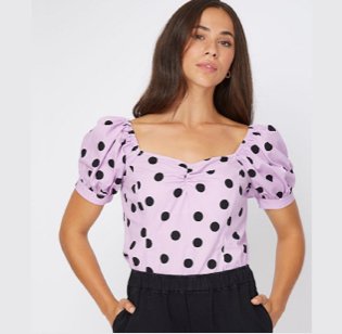 Brunette woman posing with hands in pockets wearing pink and black polka dot bardot top and black jeans.