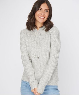 Brunette woman smiling wearing grey hoodie and light blue jeans.