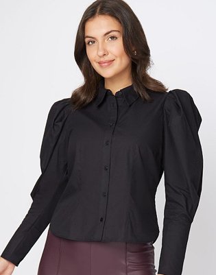 Brunette woman poses wearing black poplin puff sleeve shirt and burgundy PU trousers.
