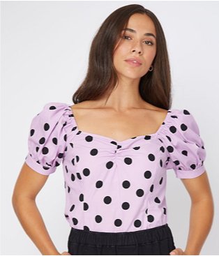 Brunette woman poses wearing lilac polka dot print blouse with balloon sleeves.