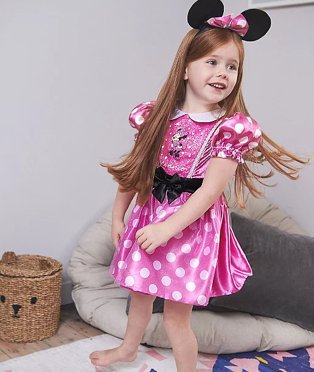 Girl poses standing on bed wearing Disney Mickey Mouse Pink Fancy Dress Costume.