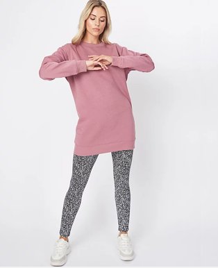 Woman with long blonde hair poses with hands together wearing pink longline sweatshirt, Noisy May black and white leopard print leggings and white pumps.