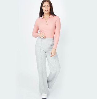 Woman with long brunette hair poses wearing peach cable knit zip neck jumper, grey marl pintuck wide leg trousers and white pumps.