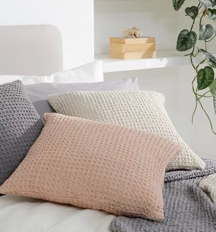 Just Wellness pink, cream and grey waffle texture cushions scattered on bed.