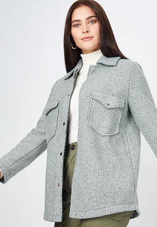 Woman poses wearing white roll neck top, khaki cargo trousers and grey bouclé shacket.