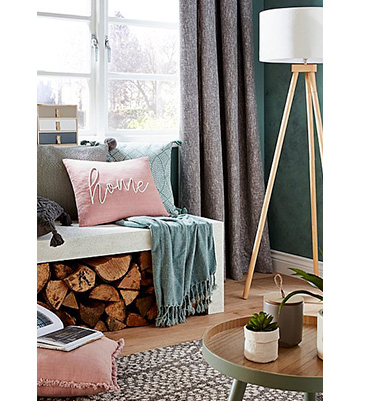 A window seat layered with cushions and a throw with a floor lamp on the side 