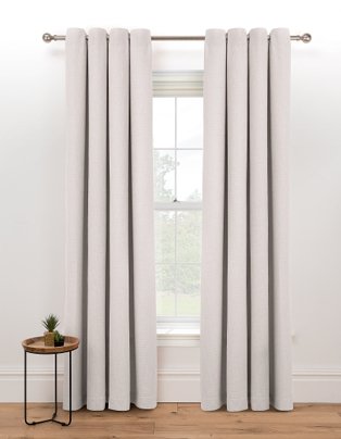 Large white window features natural eyelet curtains hanging from bronze-tone curtain rail.