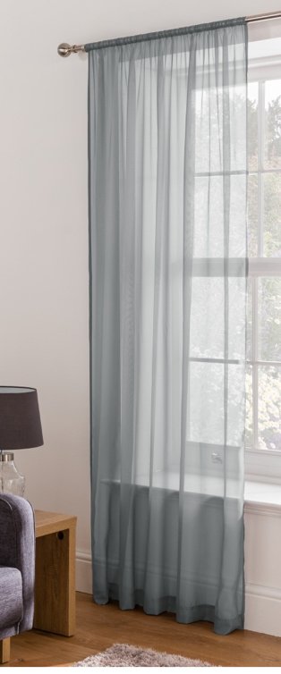 Large white window features grey voile panel hanging from gold-tone curtain rail.