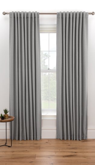 Large white window features grey eyelet curtains hanging from bronze-tone curtain rail.