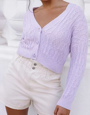 Woman poses wearing lilac patterned knit cropped cardigan and cream ruched waist shorts.