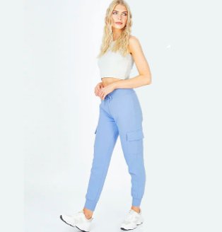 Woman poses taking one step forward wearing grey ribbed crop top, blue cargo joggers and white trainers.