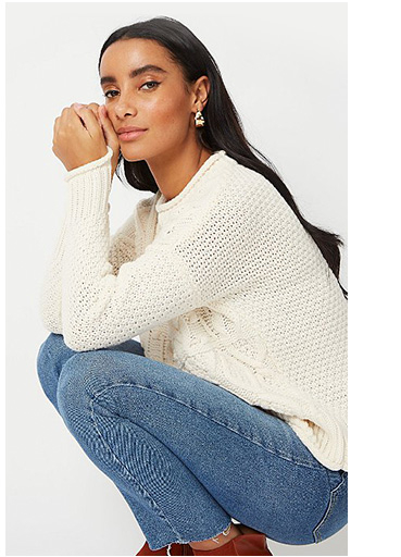 Woman crouching down wearing a cream knitted jumper and jeans