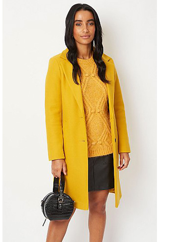 Woman wearing an ochre coloured jumper with matching longline coat and black faux leather skirt with matching handbag