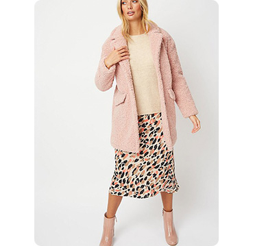 Woman wearing pink teddy fleece coat, beige top and animal print skirt with pink boots