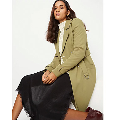 Woman wearing a green trench coat over a jumper and black skirt