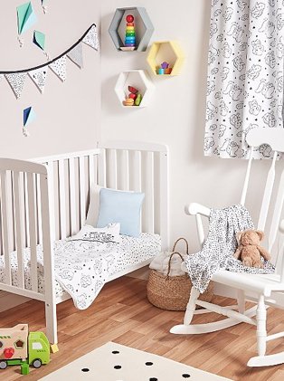 White baby nursery features white Rafferty cot bed with Disney Dumbo bedding, white rocking chair, bunting and monochrome polka dot rug.