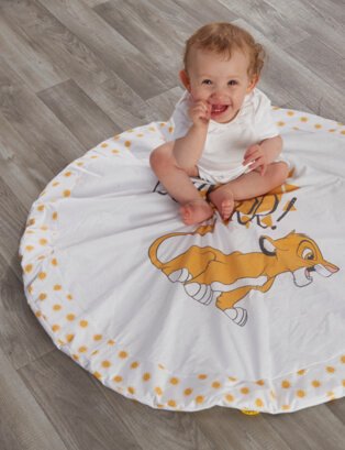 Smiling baby wearing white bodysuit sits on Lion King circle blanket.