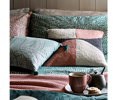 Textured cushions on a bed with a mug and sugar pot