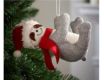 Knitted sloth hanging from a Christmas tree wearing a red scarf and Santa hat