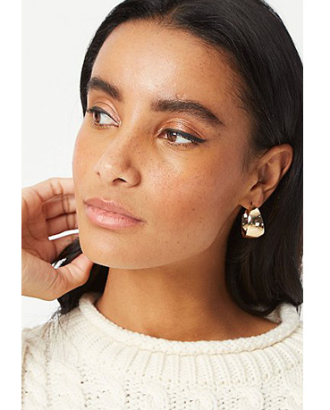 Close up shot of woman looking to the side wearing a cream jumper and hoop earrings