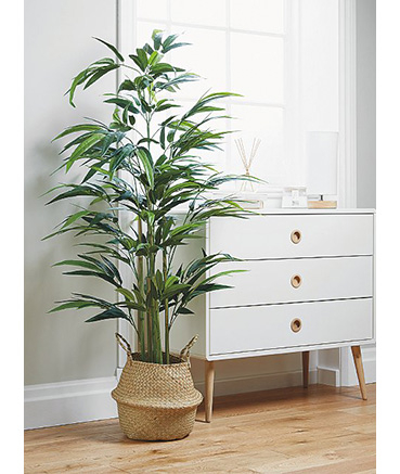 Large artificial plant in wicker planter next to a set of white drawers