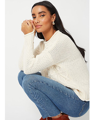 Woman crouched down wearing a cream knitted jumper and blue jeans