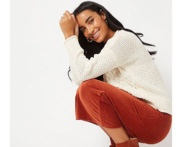 Woman kneeling down wearing a cream jumper and orange skirt 