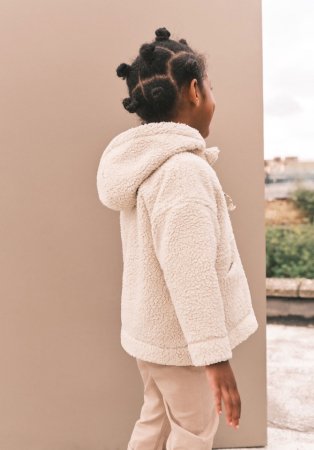 Child wearing fluffy cream jumper and beige trousers.