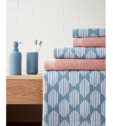 Pink and blue patterned towels on a wooden bathroom counter next to a matt blue dispenser and tumbler