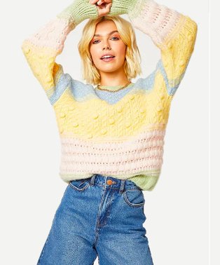 Woman poses with hands above head wearing multicoloured textured knit baloon sleeve jumper tucked into blue high-rise jeans.