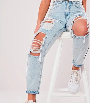 Legs of woman sitting on white chair wearing Missguided light denim distressed mom jeans.