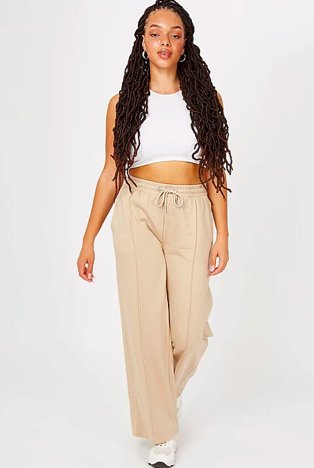 Woman walks towards camera wearing white crop top, cream wide leg pleated front elasticated joggers and white trainers.