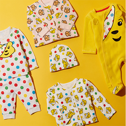 Bird's-eye view of Children in Need Pudsey Bear clothing, including a baby all in one and hat