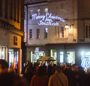 People gather at Bath Christmas Markets below illuminated Christmas signs.