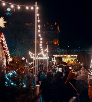 People wearing coats and hats gather at night at Edinburgh Christmas Markets.