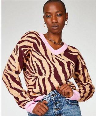 Woman poses wearing brown and cream contrast trim animal print jumper over mid blue jeans.