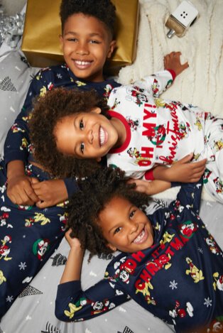Three children lay on bed smiling wearing Disney Mickey and friends sibling Christmas pyjamas.