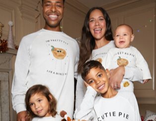 Man, woman and three children huddle together smiling wearing mince pie print matching family Christmas pyjamas.