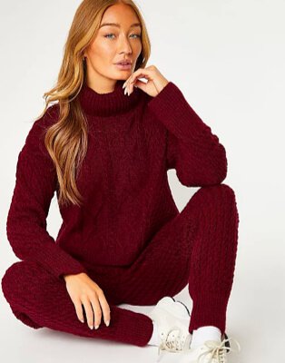Woman sits on floor wearing burgundy knitted lounge set and cream trainers.