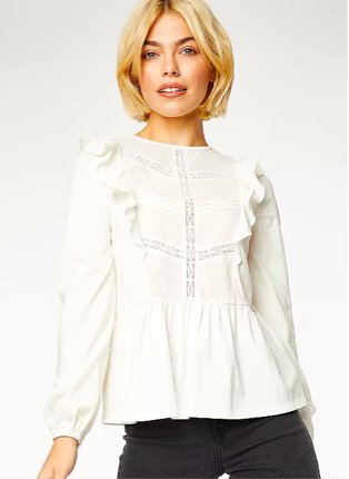 Woman poses wearing white lace ruffle front peplum blouse over black slim-fit jeans.